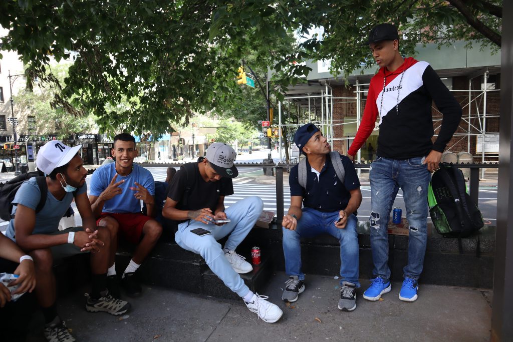 Five young men sit on a New York City street, drinking Pepsi and chatting.