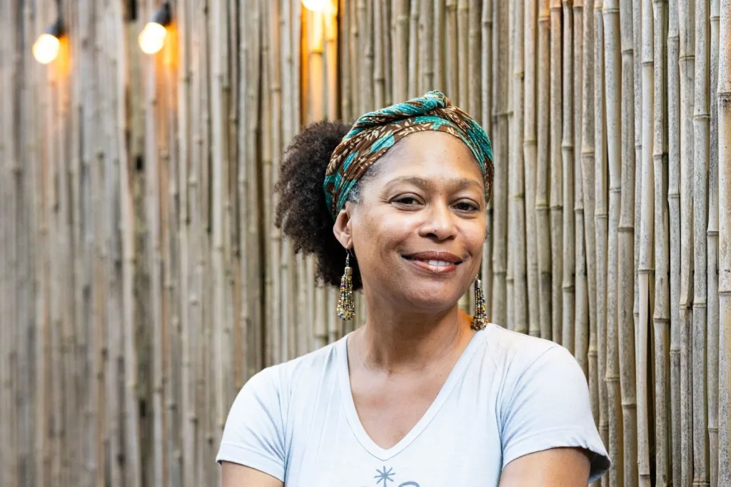 Co-founder of Haiti Cultural Excahnge, Regine Roumain, smiles in front of a bamboo wall.