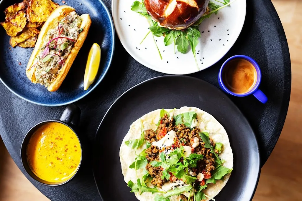 Four plates of plant-based Caribbean food seen from above.